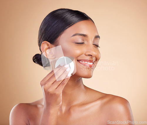 Image of Smile, makeup or happy woman with cotton pad in studio isolated on beige background for facial skincare. Glowing natural beauty or beautiful young Indian girl cleaning for self care or face wipes