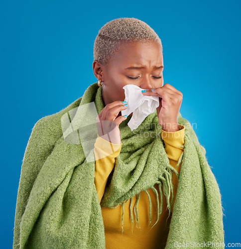 Image of Sick black woman, tissue and blowing nose in studio, blue background or hayfever allergies, cold or winter virus. Female model, sneeze and influenza allergy of health problem, covid risk or sinusitis