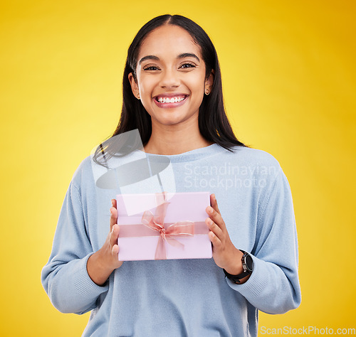 Image of Happy woman, portrait and gift box in a studio with a smile from surprise present for birthday. Giveaway prize, isolated and yellow background of a young female student feeling positive and cheerful