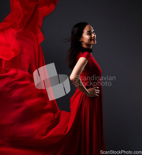 Image of Happy woman, art and fashion, red fabric on dark background with beauty and aesthetic movement. Flowing silk, fantasy and artistic model with smile in creative designer dress in studio with motion.