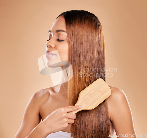 Image of Brushing hair, beauty and woman with growth and shine for healthy texture on a brown background. Face of aesthetic female in studio with a brush for natural salon keratin treatment haircare results