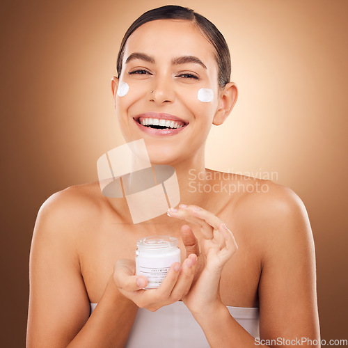 Image of Portrait, skincare and cream with a model woman in studio on a brown background for beauty or hydration. Face, beauty and product with a happy young female holding a container to apply moisturizer