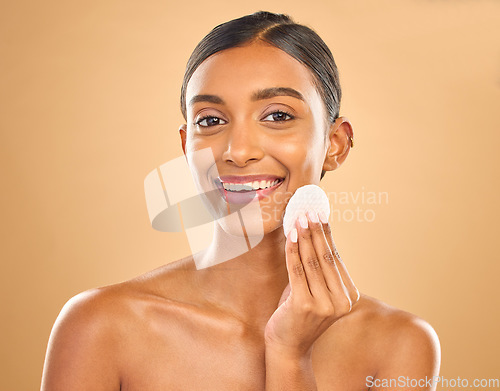 Image of Skincare, happy and portrait of woman with cotton for facial cleansing isolated on a background. Smile, beauty and an Indian model cleaning her face with a pad for gentle treatment and makeup removal