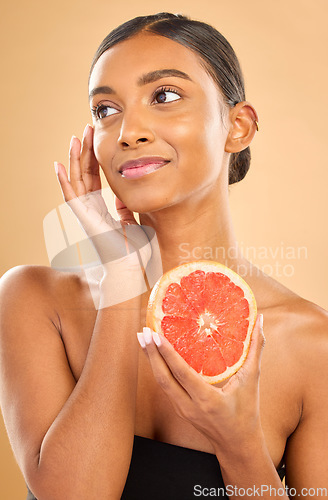 Image of Skincare, beauty and woman with a grapefruit for a glow isolated on a studio background. Thinking, smile and an Indian model with a fruit for healthy skin, complexion and vitamin c treatment