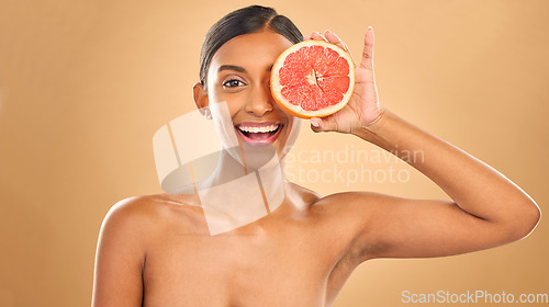 Image of Face smile, skincare and woman with grapefruit in studio isolated on a brown background. Portrait, natural cosmetics and happy Indian female model with citrus fruit for vitamin c, nutrition or beauty