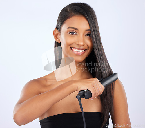 Image of Haircare, beauty and woman with a straightener in studio for a straight, long and healthy hairstyle. Happy, smile and portrait of a female model with flat iron after hair treatment by gray background