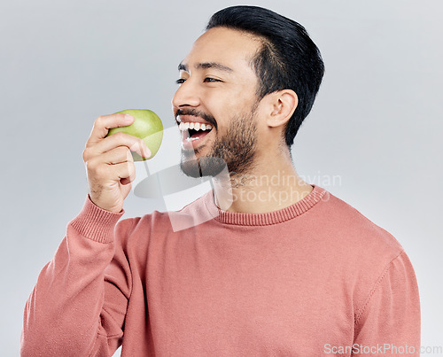 Image of Healthy, happy and an Asian man eating an apple isolated on a white background in a studio. Smile, food and a Chinese guy taking a bite from a fruit for nutrition, diet or hungry on a backdrop