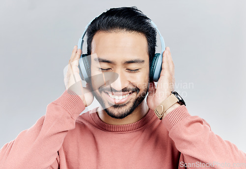 Image of Happy, music and Asian man with headphones, streaming and cheerful on a grey studio background. Japan, male and confident guy with headset, listening to audio and sounds for peace, smile and wellness