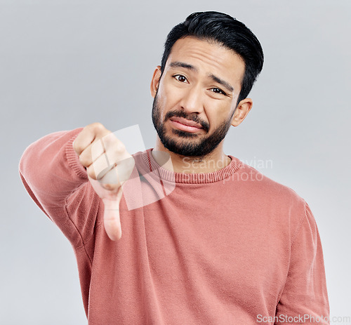 Image of Sad, disappointment and portrait of an Asian man with a thumbs down isolated on a studio background. Review, unhappy and a Chinese guy with a hand sign for a problem, mistake and dislike emoji