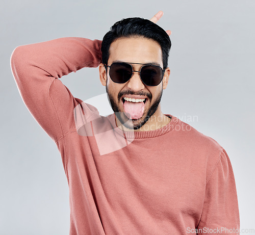 Image of Portrait, tongue out and Asian man with sunglasses, funny and silly against a grey studio background. Face, Japanese male and guy with funky eyewear, shades and comic with humor and goofy expression