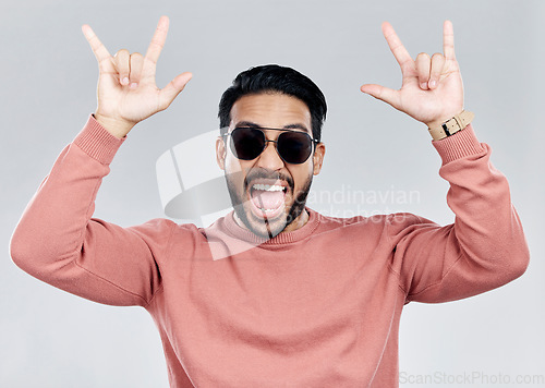 Image of Portrait, rocker and hand gesture with a man in studio on a gray background feeling crazy or energetic. Face, rock on or hardcore and a male posing with a devil horns sign or symbol at a concert