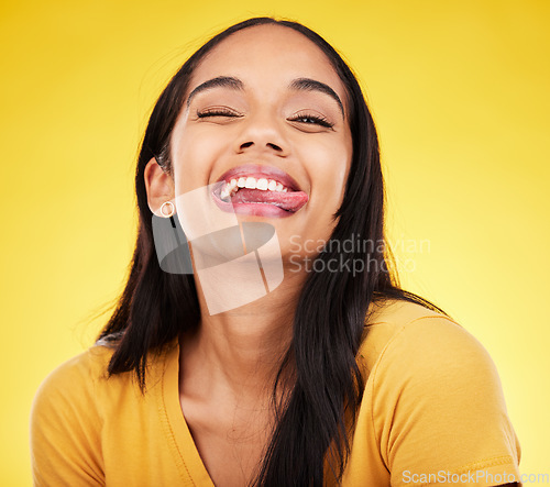 Image of Woman, portrait smile and tongue out with silly facial expression against a yellow studio background. Happy, fun and goofy carefree female model smiling with teeth and funny face in joyful happiness