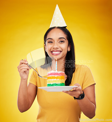 Image of Woman is eating birthday cake, celebration and happy in portrait, rainbow dessert and candle on yellow background. Celebrate, festive and young female, excited for sweet treat and party hat in studio