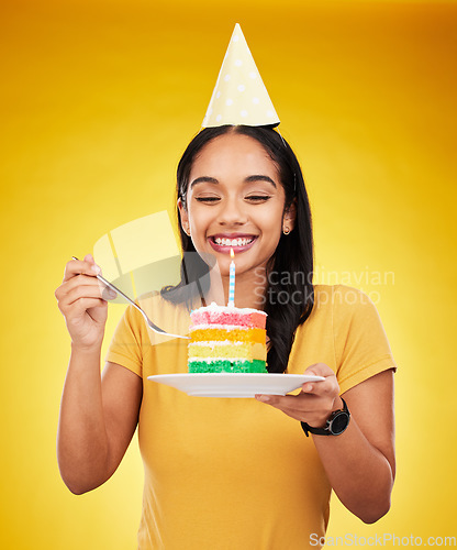Image of Woman is eating cake, birthday celebration and happy in portrait, rainbow dessert and candle on yellow background. Celebrate, festive and young female, excited for sweet treat and party hat in studio
