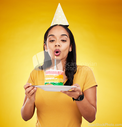 Image of Woman, birthday cake and celebration, blow out candle with rainbow dessert isolated on yellow background. Celebrate, festive and young female, making a wish with sweet treat and party hat in studio