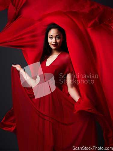 Image of Woman, art and fashion, red fabric on dark background with beauty and aesthetic movement. Flowing silk motion, fantasy and artistic portrait of model with smile in designer dress and veil in studio