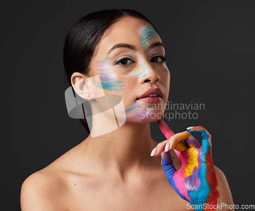 Image of Woman, beauty and portrait with rainbow hand paint art on face in studio with glow. Creative skin and makeup on female aesthetic model serious on gray background for lgbtq color inspiration on hands