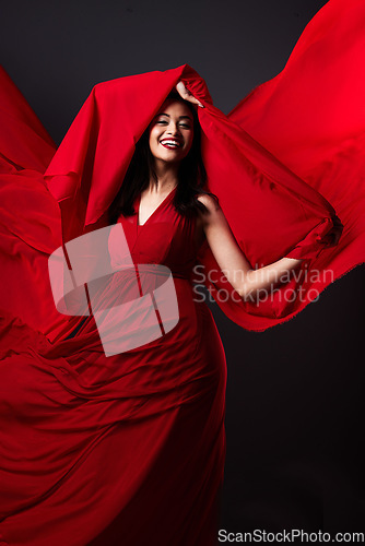 Image of Woman, beauty and fashion, red art on dark background with energy and aesthetic movement. Flowing silk motion, fantasy and artistic model with smile in creative fabric designer dress in studio