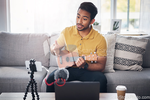 Image of Podcast, guitar and phone with a man online to talk and coach during live streaming lesson. Asian male person talking on home sofa with a ukulele as content creator teaching music on education blog