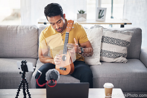 Image of Guitar, podcast and phone with a man online teaching, show and coach on live streaming lesson. Asian male person happy on home sofa with a ukulele as content creator teaching music on education blog