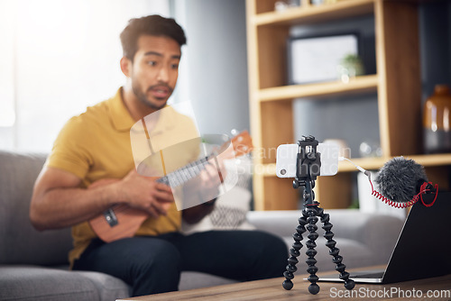 Image of Podcast microphone, phone and guitar with a man online to coach during live streaming lesson. Asian male influencer on home sofa with a ukulele as content creator teaching music on education blog