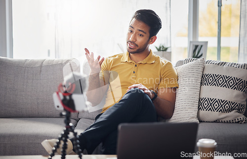 Image of Content creator, laptop and phone, Indian man on sofa recording webinar, broadcast and live streaming in home. Internet, webcam and online influencer talking with equipment for social media channel.