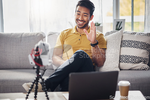 Image of Laptop, phone and content creation, Indian man on sofa, webinar recording and live streaming in home. Internet, webcam and online influencer with smile, wave and equipment for social media channel.