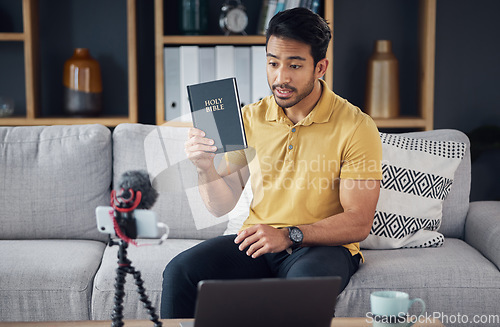 Image of Streaming, bible and man talking on phone and microphone online for live podcast. Asian male on home sofa with Christian religion book as blog content creator or influencer teaching or studying