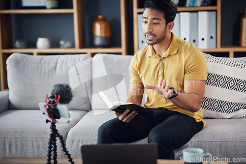 Image of Book, bible study and phone with a man online to preach or reading while live streaming. Asian male on home sofa talking Christian scripture as podcast content creator teaching education on religion