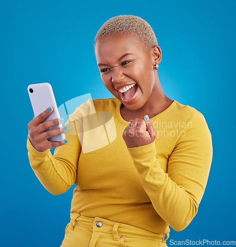 Image of Black woman, phone and fist celebration in studio, blue background and winning online prize. Happy female model celebrate mobile promotion, bonus and excited for deal, success and competition winner