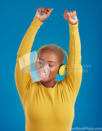 Image of Black woman with headphones, dance and listening to music with rhythm and fun with freedom on blue background. Happy female with arms raised, streaming radio with dancing and carefree in studio