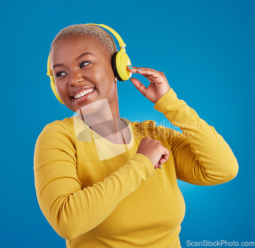 Image of Black woman, headphones and listening to music with a smile in studio while happy streaming audio. African female model on a blue background to listen to radio, podcast or sound with a positive mood