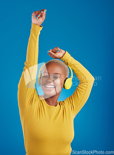 Image of Black woman with headphones, dance and listen to music with rhythm and fun with freedom on blue background. Happy female with arms raised, streaming radio with dancing and carefree in studio