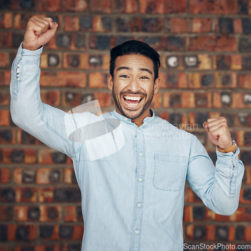 Image of Portrait, winner and motivation with a man in celebration against a brick wall background enjoying victory. Energy, wow and success with a handsome young man celebrating an achievement or bonus