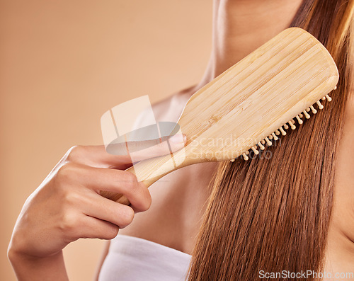 Image of Hairbrush, hair care and woman brushing her hair in a studio for wellness, health and self care. Cosmetic, beauty and closeup of a female model doing a hairstyle or combing knots by brown background.