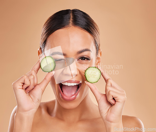 Image of Skincare, wink and portrait of woman with cucumber in hands for wellness, facial treatment and natural cosmetics. Beauty, spa and happy girl with fruit for detox, vitamin c and healthy skin in studio