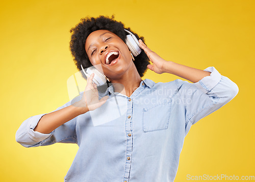Image of Black woman, headphones and freedom, listening to music and happiness with dance on yellow studio background. Happy female, carefree and sing along to radio, audio streaming with fun and technology