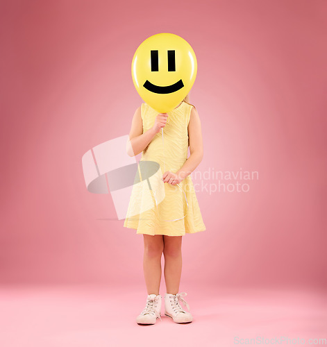 Image of Smiley face, balloon and child in studio, covering and hiding against a pink background space. Happy, emoji and girl holding toy, game and playing while posing behind inflatable, fun and innocent