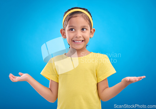 Image of Girl, child and shrug with happy or unsure face in studio with arms and hands stretched with a smile. Kid on blue background clueless, doubt and confused about question or reaction with hand gesture