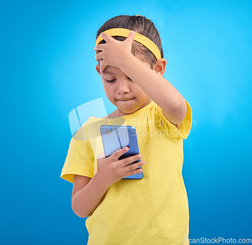 Image of Phone, face palm and a girl on a blue background in studio reading a text message or post on social media. Contact, mobile and mistake with a young female child looking at bad news on her smartphone