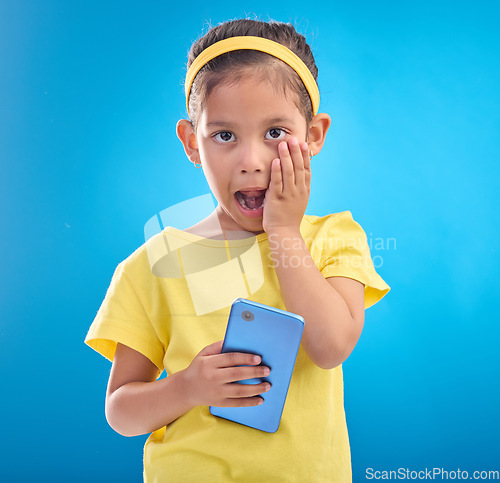 Image of Phone, shock and portrait of child on blue background with wow, omg and surprise expression in studio. Technology, childhood and face of girl shocked for news, announcement or message on smartphone