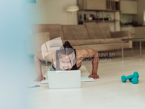 Image of Young African American man working push-ups in the living room while watching online training on laptop