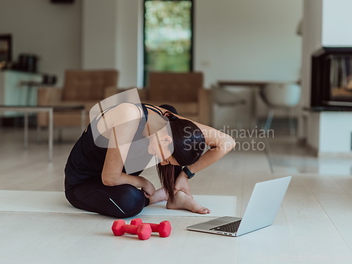 Image of A young woman in sportswear is sitting in the living room and preparing for online training while using a laptop