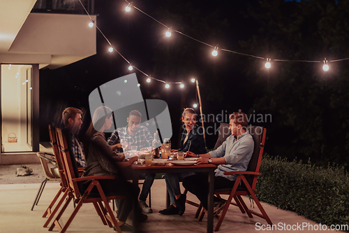 Image of A group of young diverse people having dinner on the terrace of a modern house in the evening. Fun for friends and family. Celebration of holidays, weddings with barbecue.