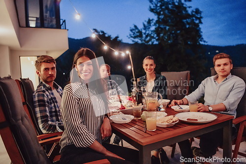 Image of A group of young diverse people having dinner on the terrace of a modern house in the evening. Fun for friends and family. Celebration of holidays, weddings with barbecue.