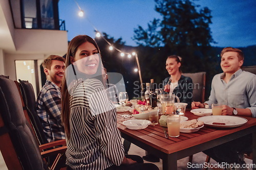 Image of A group of young diverse people having dinner on the terrace of a modern house in the evening. Fun for friends and family. Celebration of holidays, weddings with barbecue.