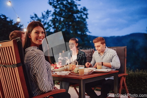 Image of A group of young diverse people having dinner on the terrace of a modern house in the evening. Fun for friends and family. Celebration of holidays, weddings with barbecue.