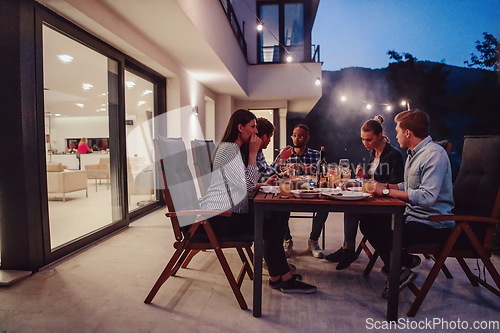 Image of A group of young diverse people having dinner on the terrace of a modern house in the evening. Fun for friends and family. Celebration of holidays, weddings with barbecue.