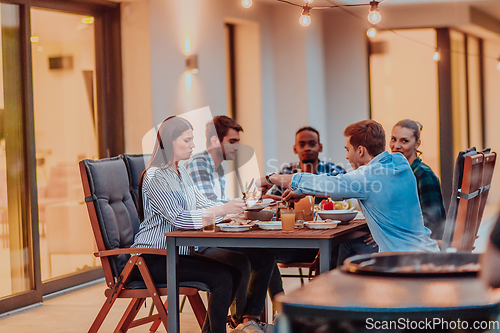 Image of A group of young diverse people having dinner on the terrace of a modern house in the evening. Fun for friends and family. Celebration of holidays, weddings with barbecue.