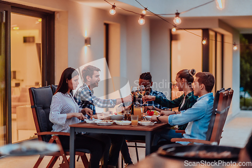 Image of A group of young diverse people having dinner on the terrace of a modern house in the evening. Fun for friends and family. Celebration of holidays, weddings with barbecue.